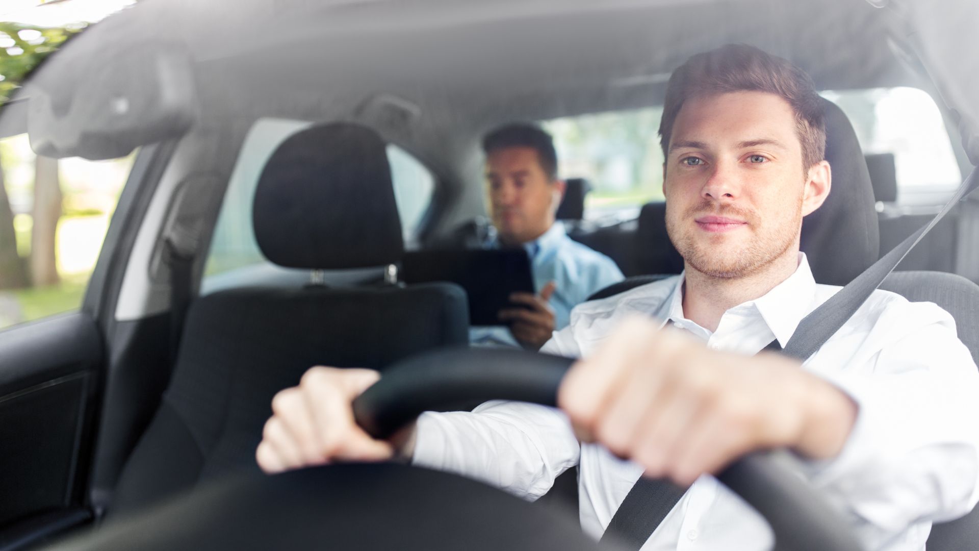 A man driving a car with another man behind him