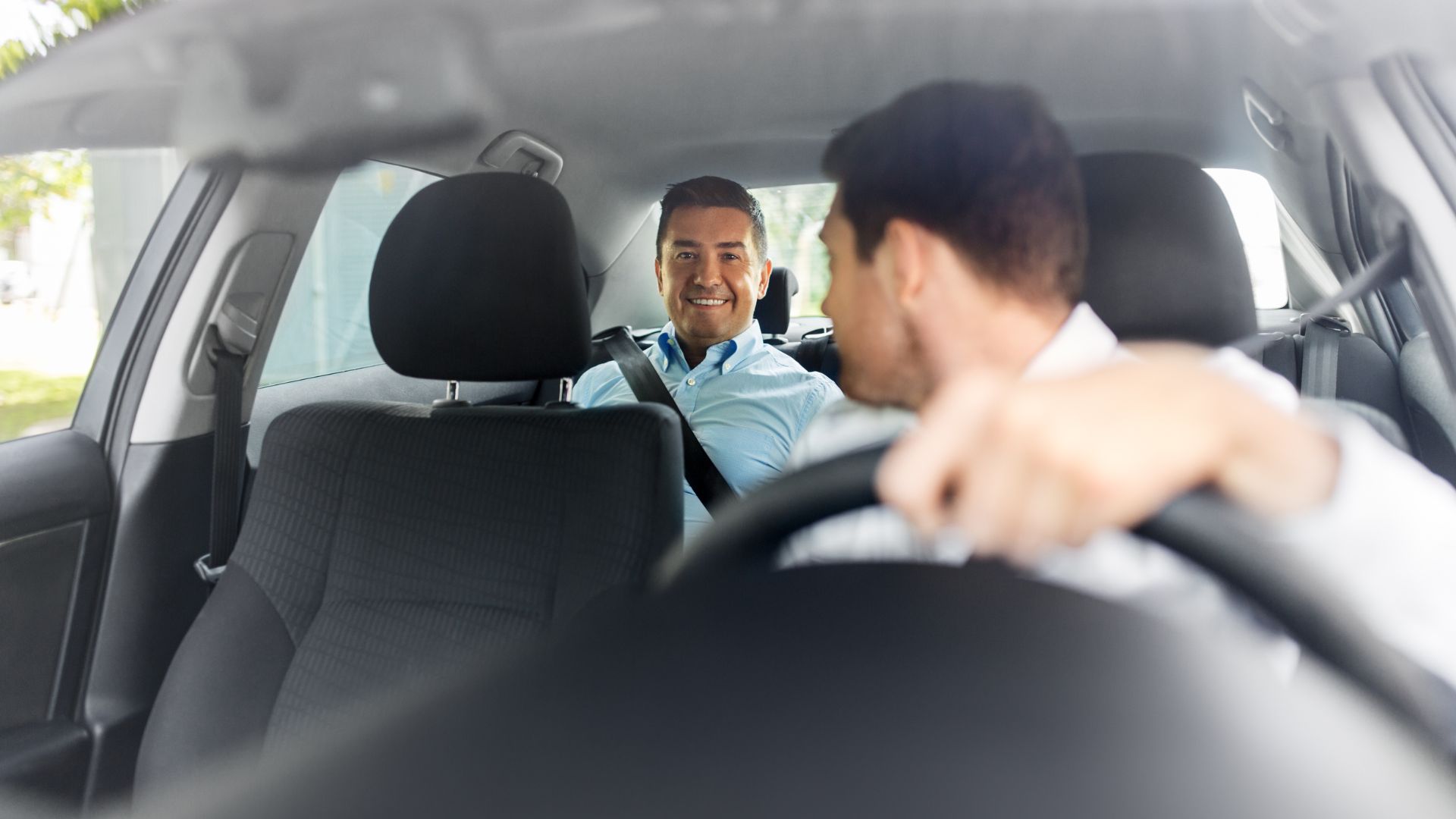 A man sitting in the back seat of a car talking to another man